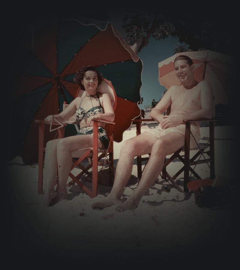 A man and a woman relax under umbrellas at the beach.