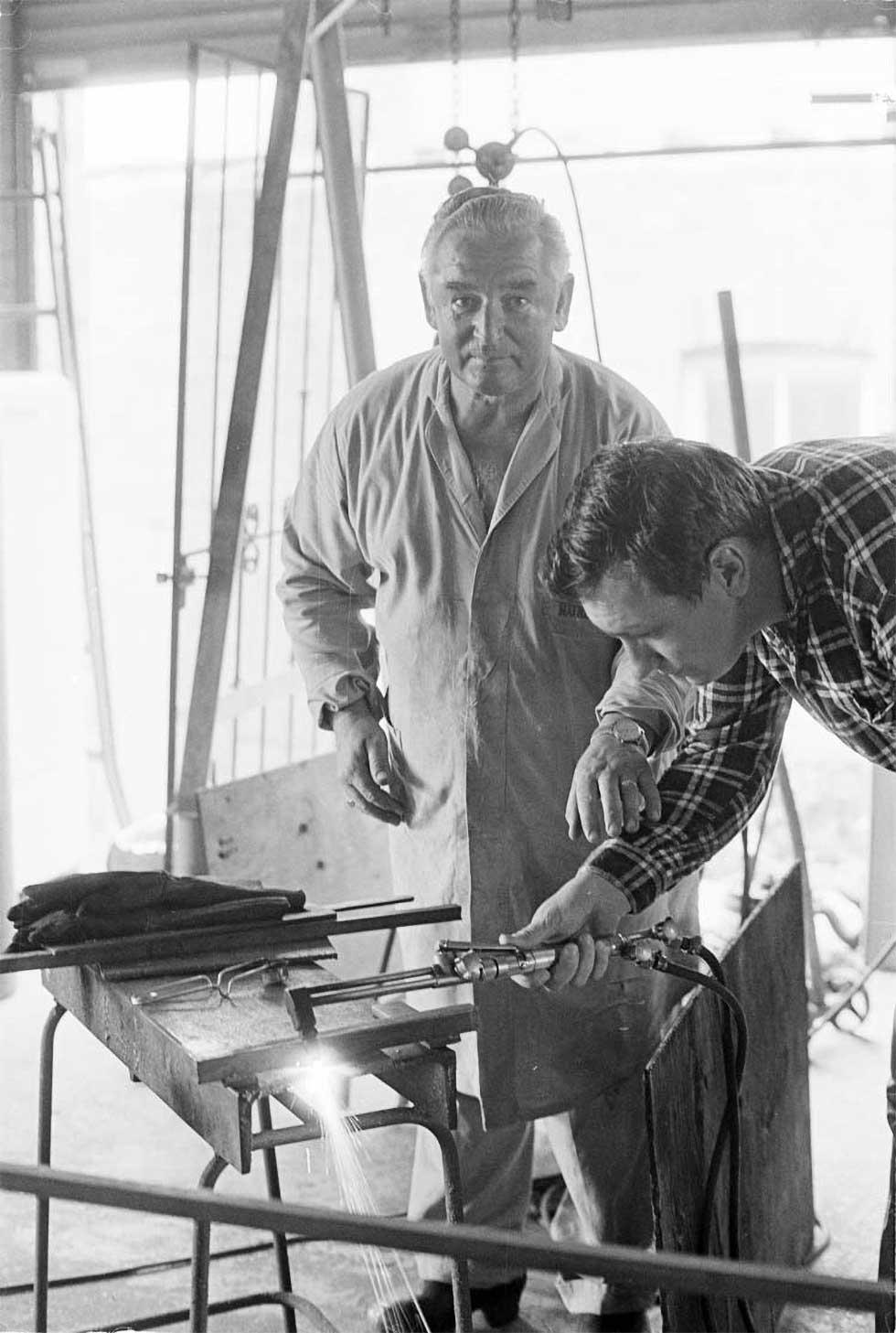 A man teaching another man to weld.