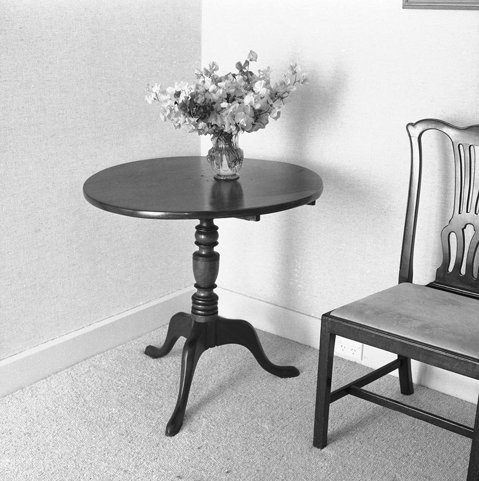 Cedar table with vase of flowers and chair in the corner of a room.