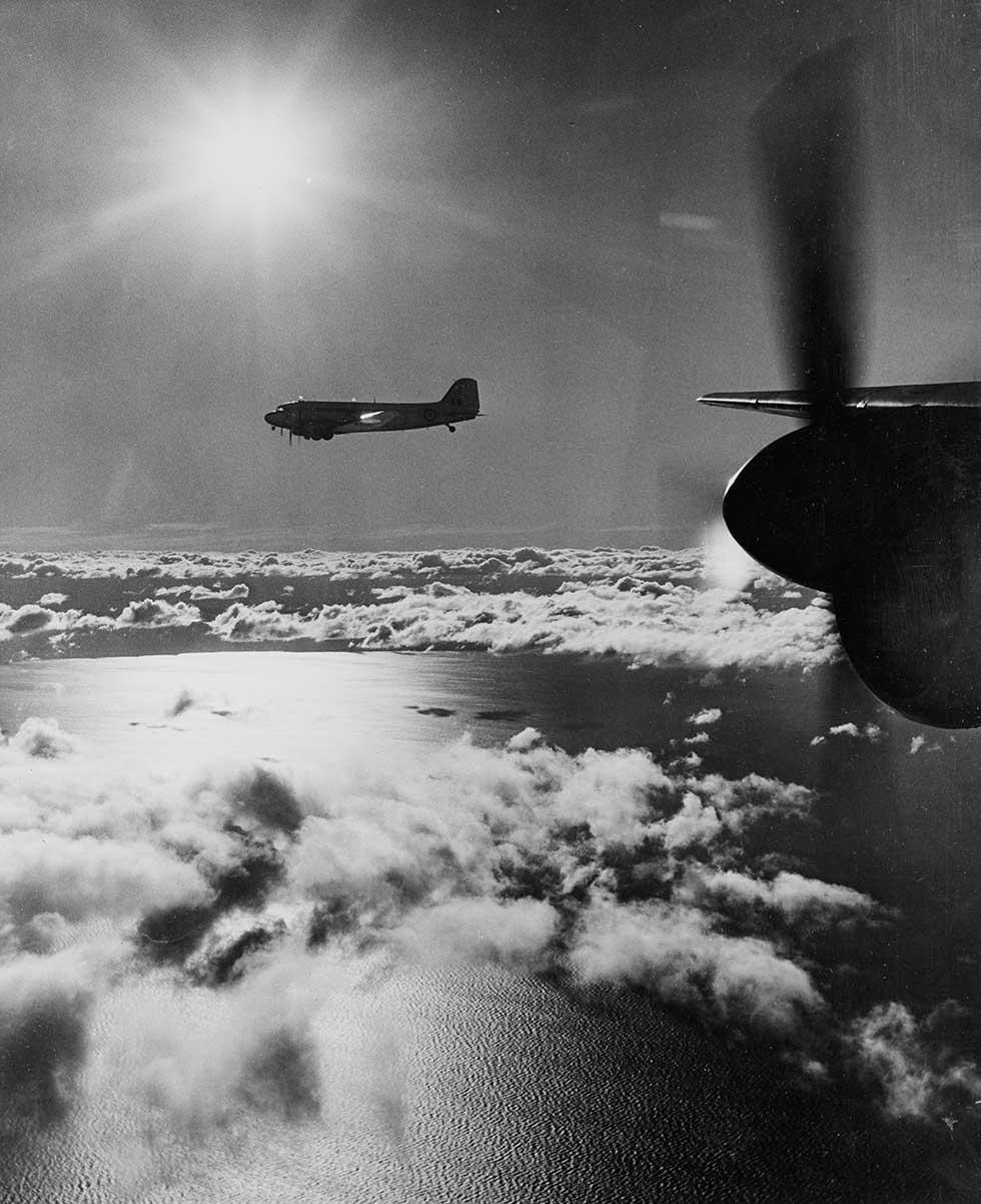 A Royal Australian Air Force DC3 aircraft flying above cloud over the coast, photographed from another DC3. 