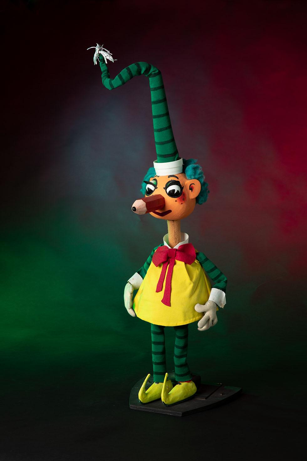 Colour photograph of Mr Squiggle, dressed in a yellow smock, red tie, green and black striped hat.