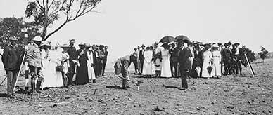 A group of formally dressed men and women watching King O'Malley knocking in the first surveyor's peg on the site of Canberra.