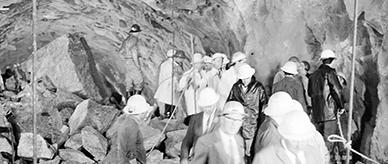 Miners and official guests picking their way through broken rocks.