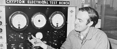 A man in overalls operating an electrical test bench.