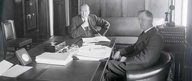 Prime Minister Bruce and James Scullin seated at a large desk.