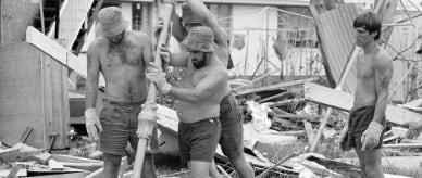 Three men erecting a Hills Hoist clothesline. Debris from Cyclone Tracey in the background.