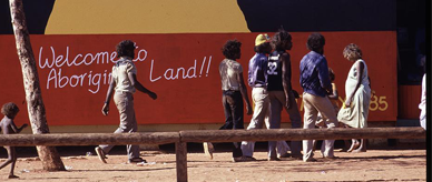People walking in front of a mural with the writing 'Welcome to Aboriginal land'