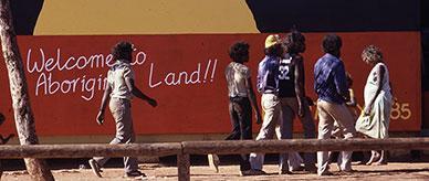 First Australians walk past a mural of the Aboriginal flag with the sun replaced by a yellow image of Uluru.