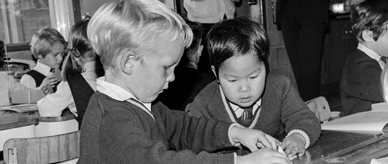 A Vietnamese war orphan and an Australian friend working at a desk in school.