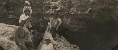 6 people and a dog seated on rock beside a cave entrance.