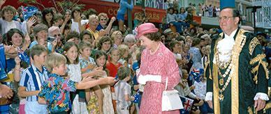 A young boy in a brightly coloured shirt reaches out to the Queen.