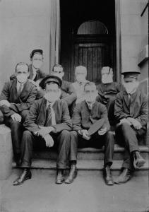 Post office workers wearing masks and sitting on steps outside while they are photographed.