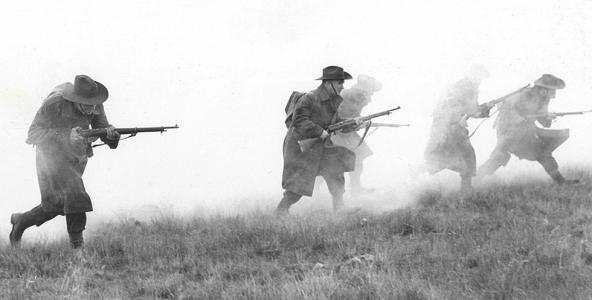 Men of the Volunteer Defence Corps armed with rifles walking across a paddock