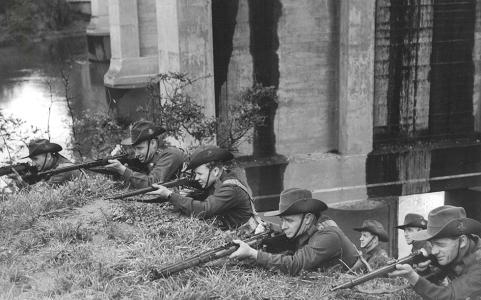 Men of the Volunteer Defence Corps armed with rifles on an embankment next to a bridge.