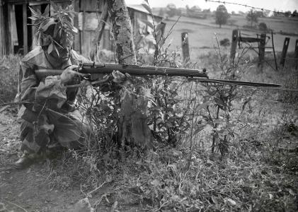 A man wearing camouflage crouching with a rifle and bayonet.