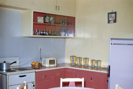 A modern kitchen with a stove, radio and yellow canisters. The drawers and shelves are dark pink.