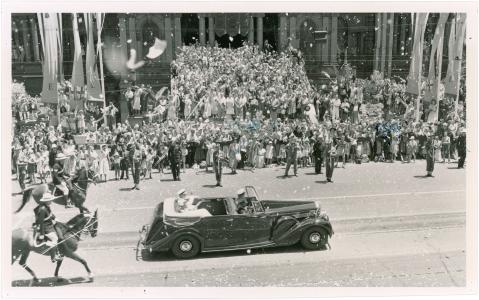 The Queen being driven past crowds in an open top Rolls Royce.
