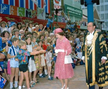 The Queen walking in front of a crowd of children. A young boy reaches out to her. 