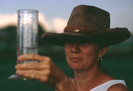 A woman wearing a hat holds a rain gauge to sight the water level
