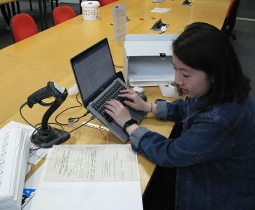 Evelyn transcribing paper file details using a laptop.