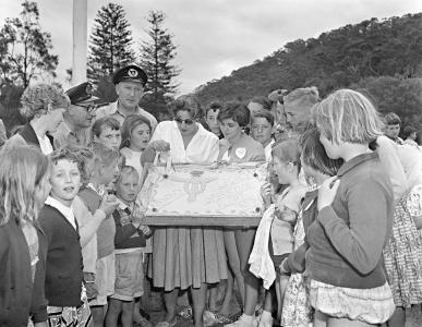 Adults and children gather around a large cake decorated by the Legacy Club Sydney.